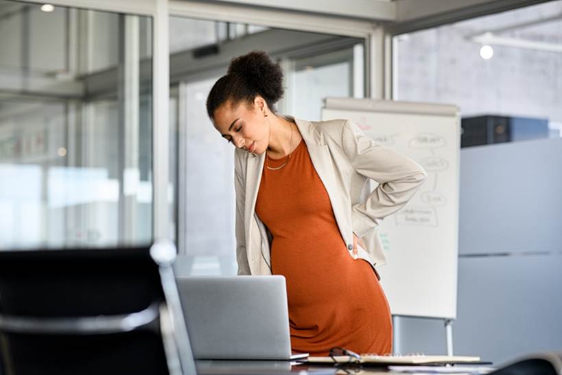 Pregnant woman holding back at work - Pregnancy Discrimination